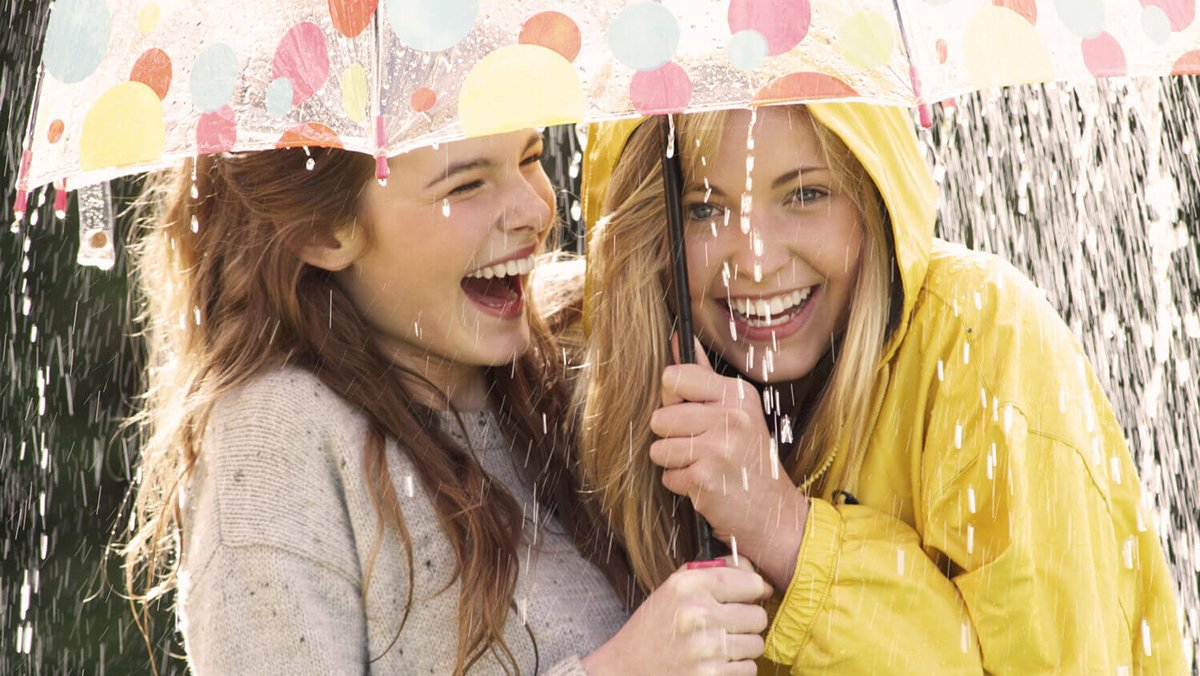 Dos mujeres jóvenes riéndose debajo de un paraguas
