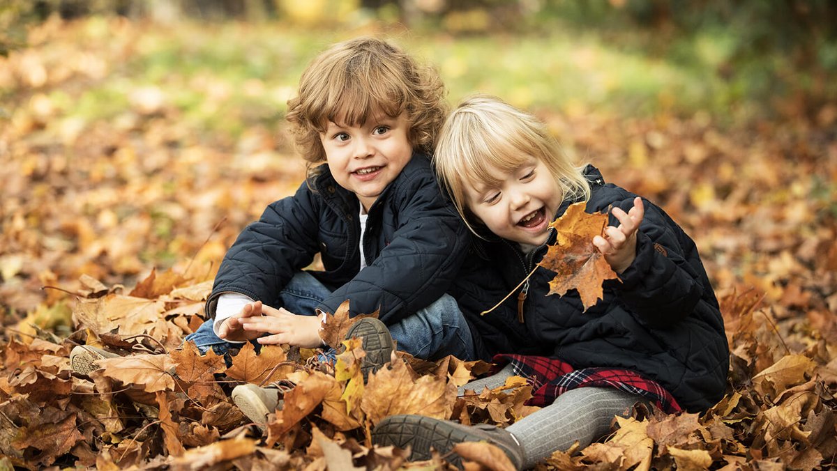 Dos niños sentados en hojas caídas de los árboles 