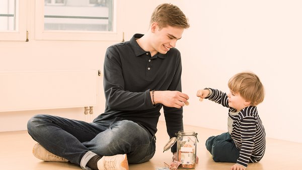 Niño y hombre joven metiendo dinero en un bote de ahorros