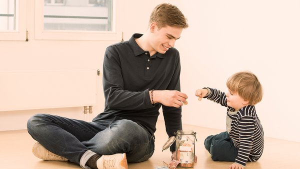 Niño y hombre joven metiendo dinero en un bote de ahorros Niño y hombre joven metiendo dinero en un bote de ahorros